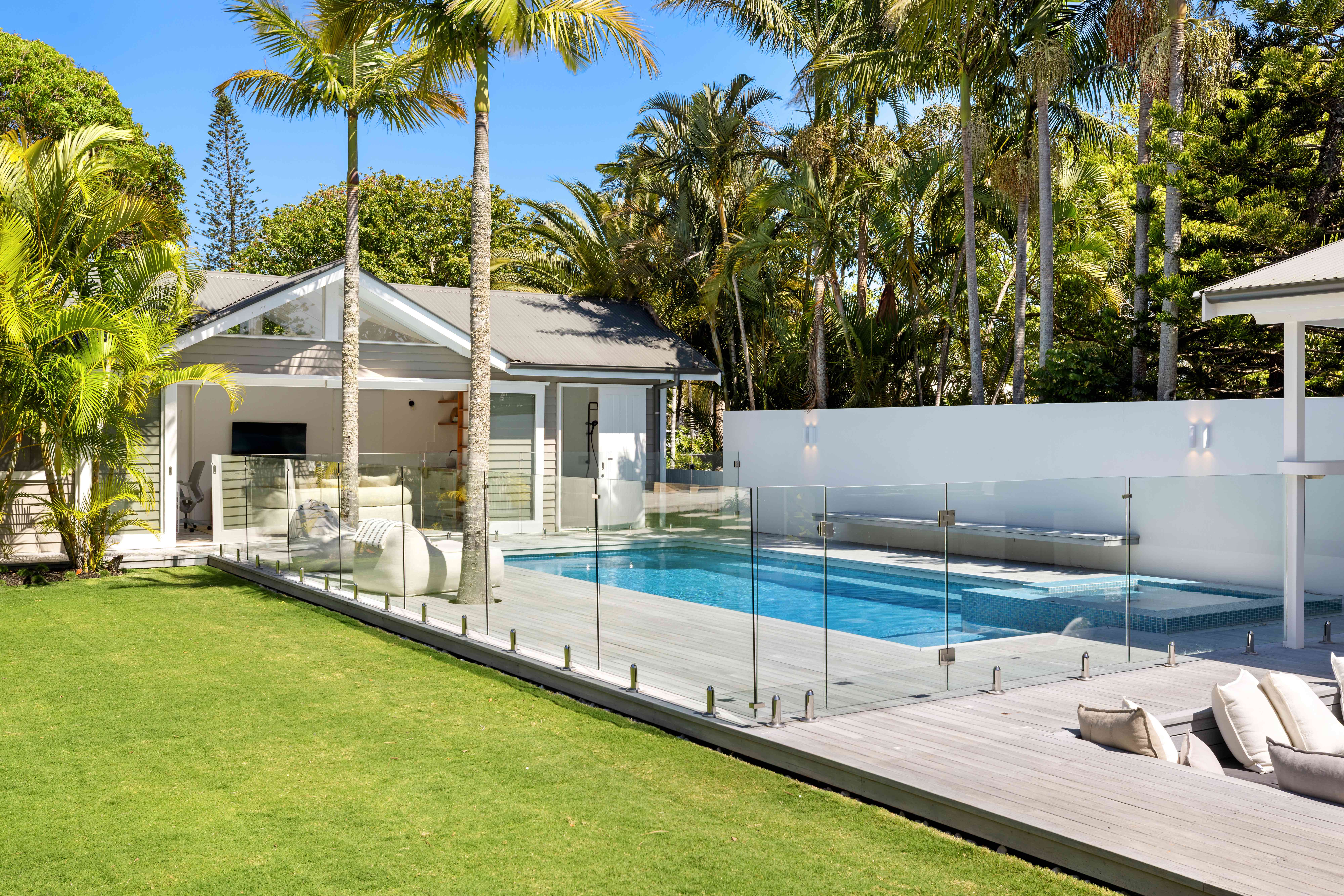 Pool and lawn view with glass fencing and palm trees
